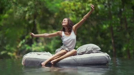 Relaxed woman sitting on air mattress in natural water setting, symbolizing comfort and sleep relaxation.