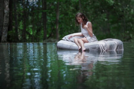 Misty forest scene with a girl sitting on an air mattress in water, natural outdoor setting, relaxing sleep on comfortable mattress, nature-inspired sleep environment, The Mattress Underground SEO.
